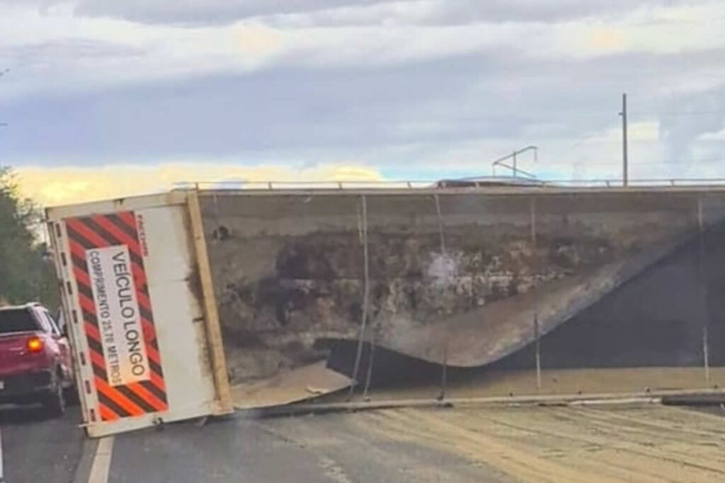 Com o caminhão tombado n meio da rodovia, apenas carros pequenos conseguem passar usando o acostamento da rodovia